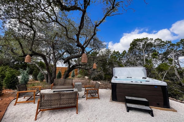 Backyard patio with hot tub, wooden deck, lounge seating, shade sail, and modern house with glass doors