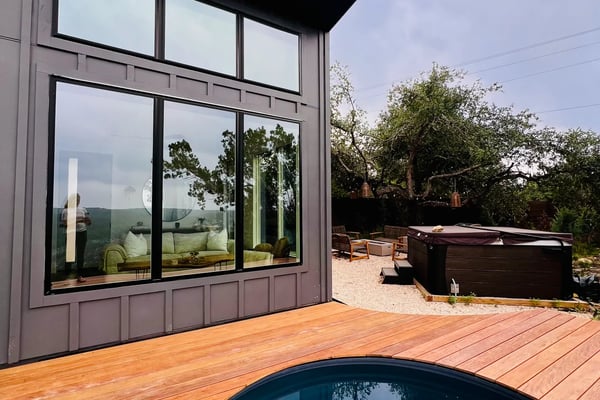 Open-plan kitchen and living room with expansive windows overlooking rolling hills and trees, black ceiling fan, pendant light, and valley views.